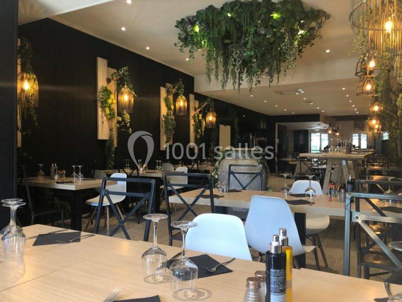 Salle de restaurant moderne avec tables dressées, chaises variées et décoration végétale suspendue.