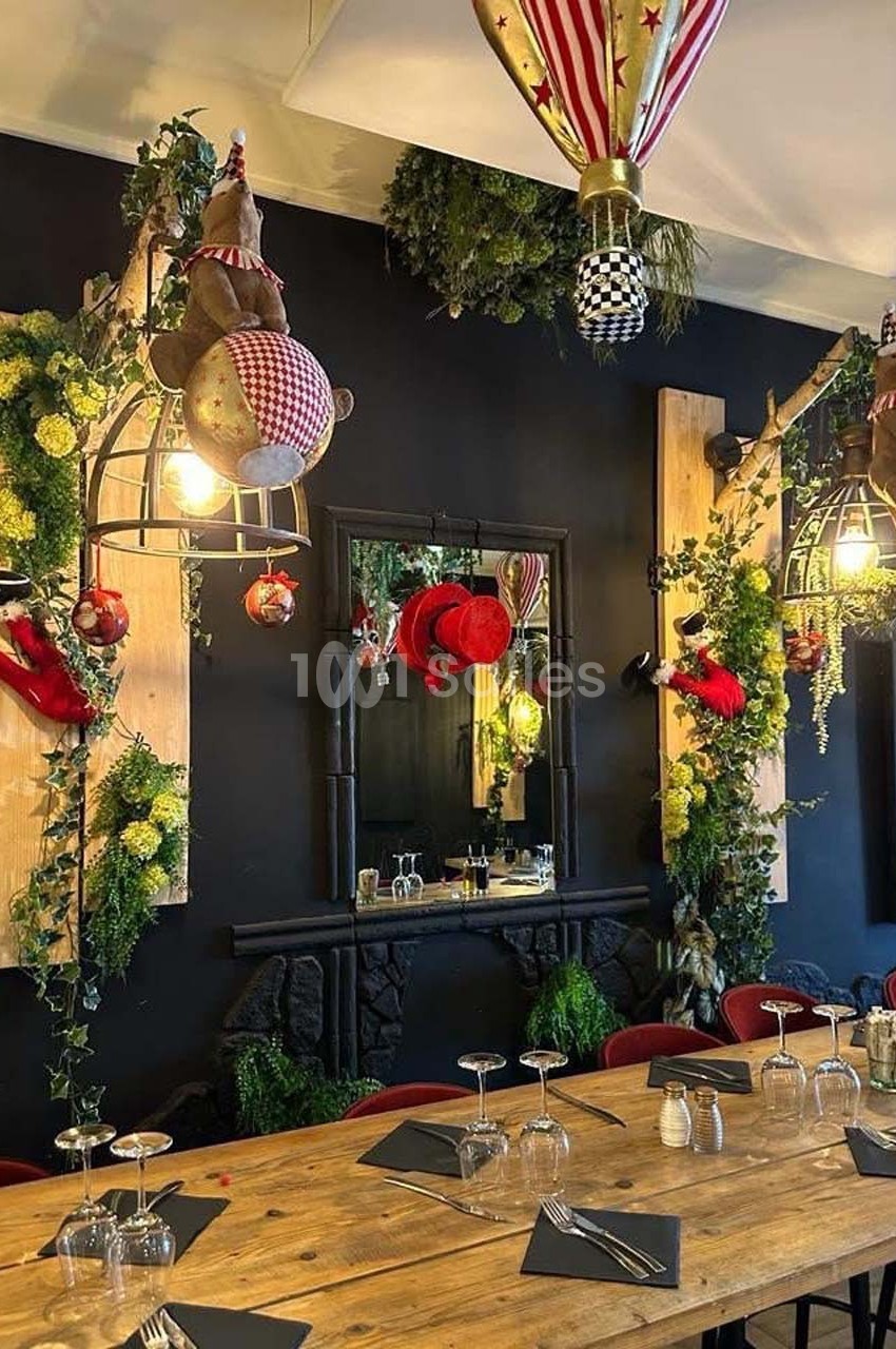 Salle à manger décorée avec des éléments festifs, des plantes suspendues et des luminaires originaux au-dessus d'une grande…