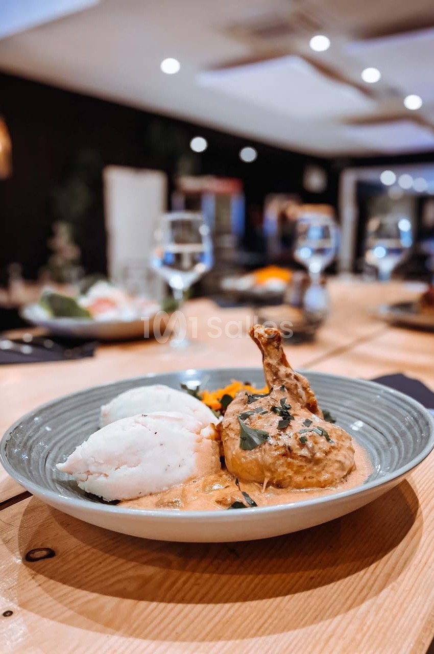 Plat de poulet en sauce avec purée et légumes, servi dans une assiette sur une table en bois dans un restaurant.