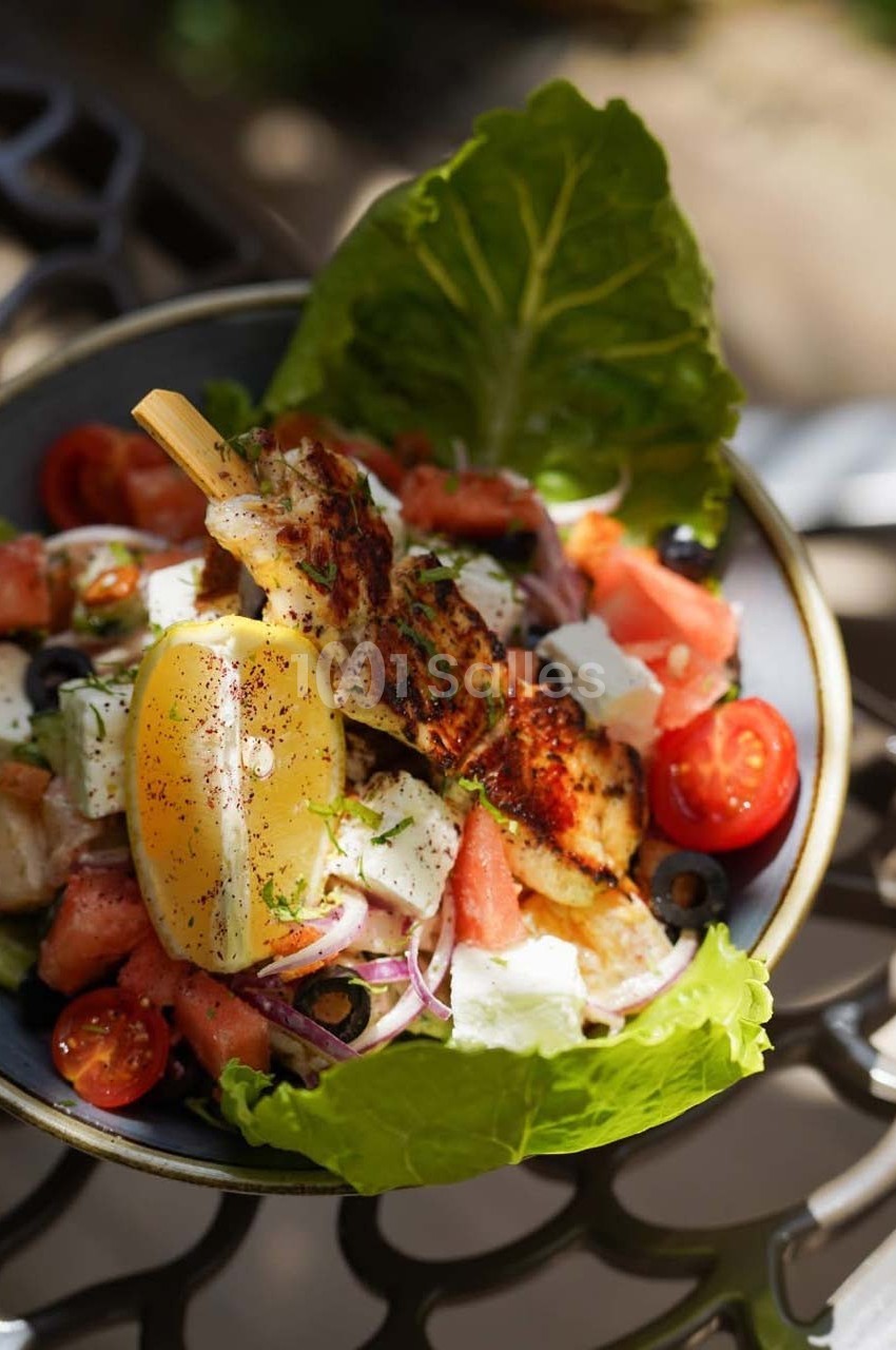 Assiette de salade grecque garnie de brochette de poulet grillé, citron, tomates cerises et feuilles de laitue.