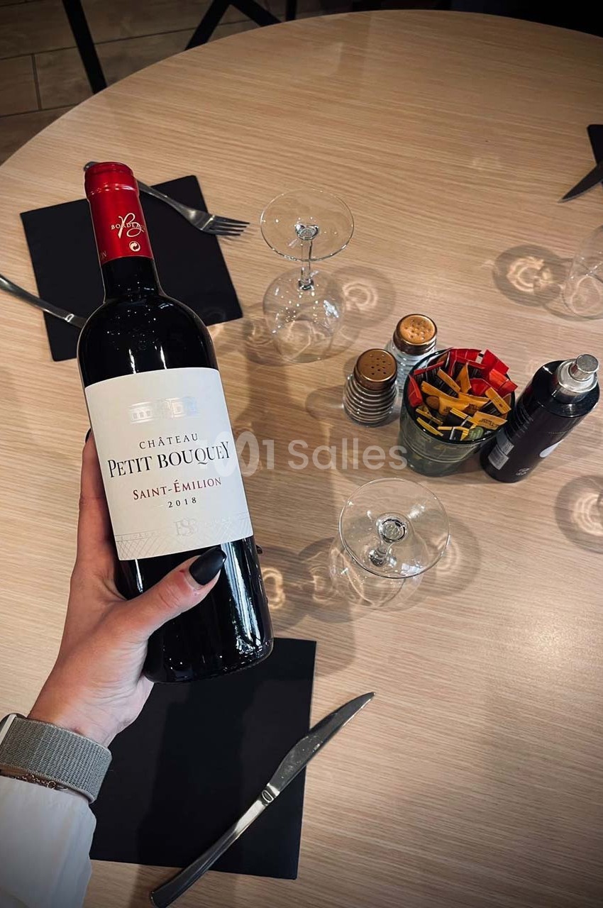 Bouteille de vin rouge Château Petit Fombrauge Saint-Émilion 2018 tenue au-dessus d'une table dressée.