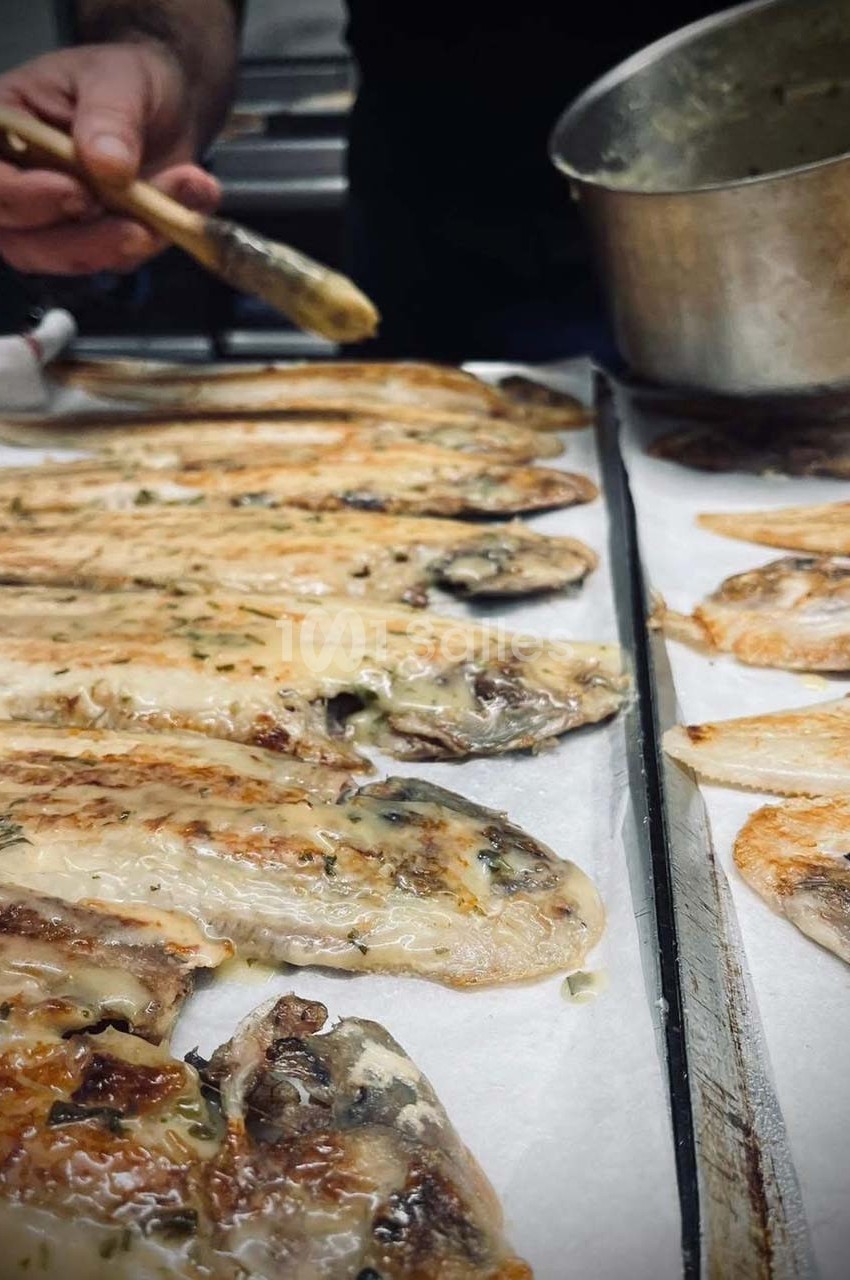 Filets de poisson grillés alignés sur du papier cuisson, avec une main appliquant une sauce à l'aide d'un pinceau.