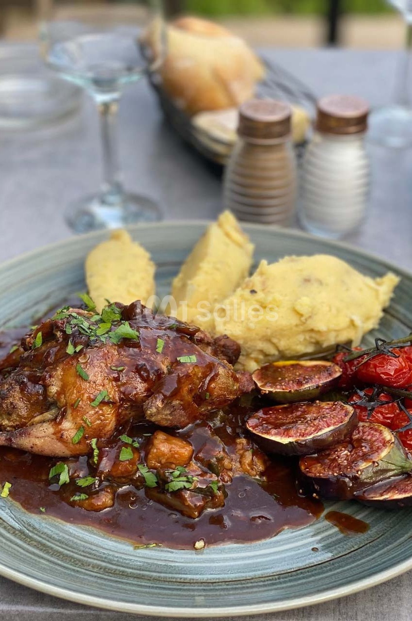 Assiette contenant du poulet en sauce, figues rôties, tomates grillées et purée, servie sur une table dressée.