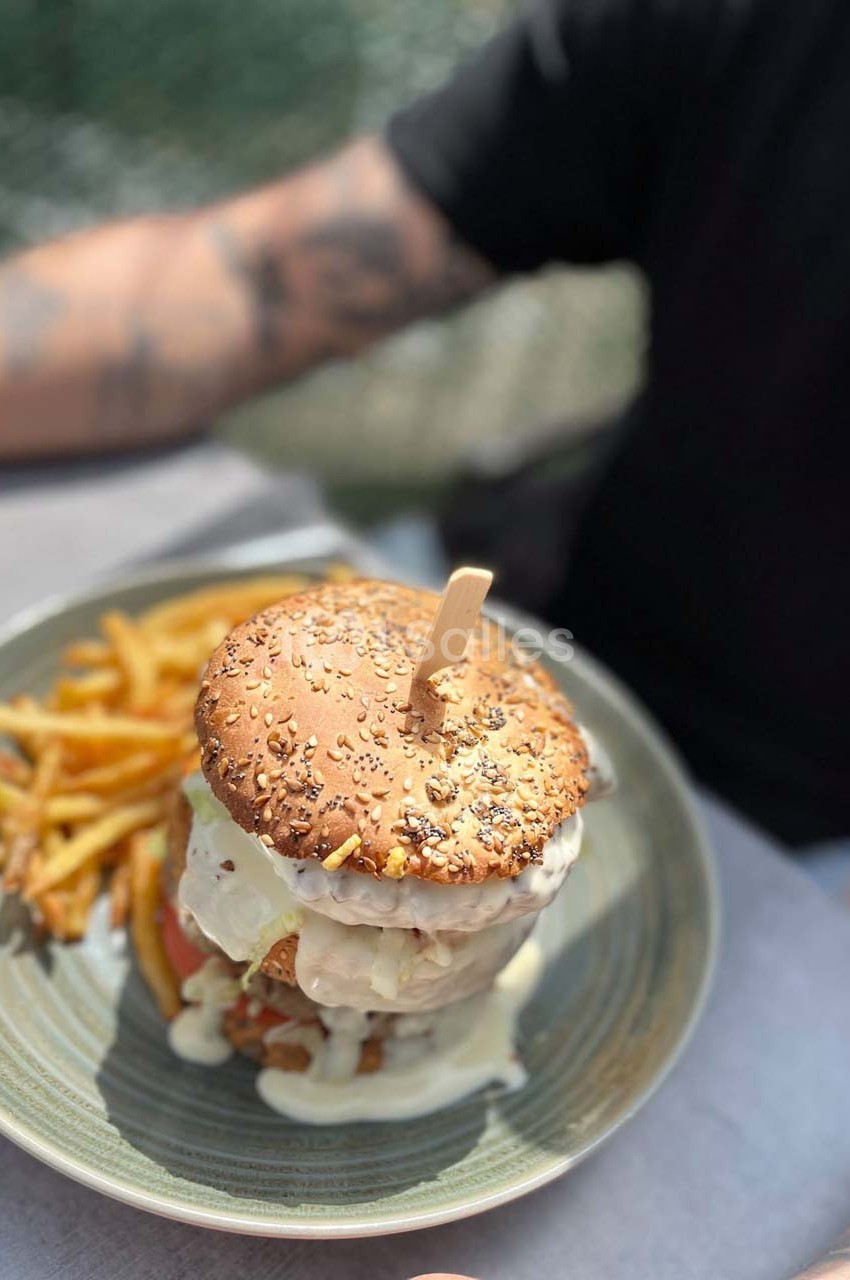 Burger garni avec sauce fondante, accompagné de frites, servi sur une assiette en extérieur.