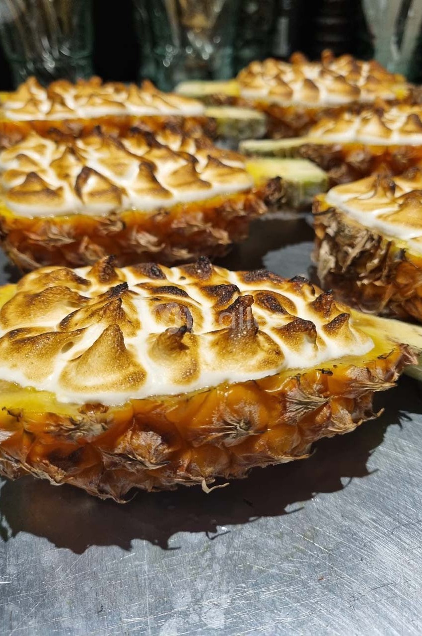 Moitiés d'ananas garnies de meringue dorée, disposées sur une surface métallique.