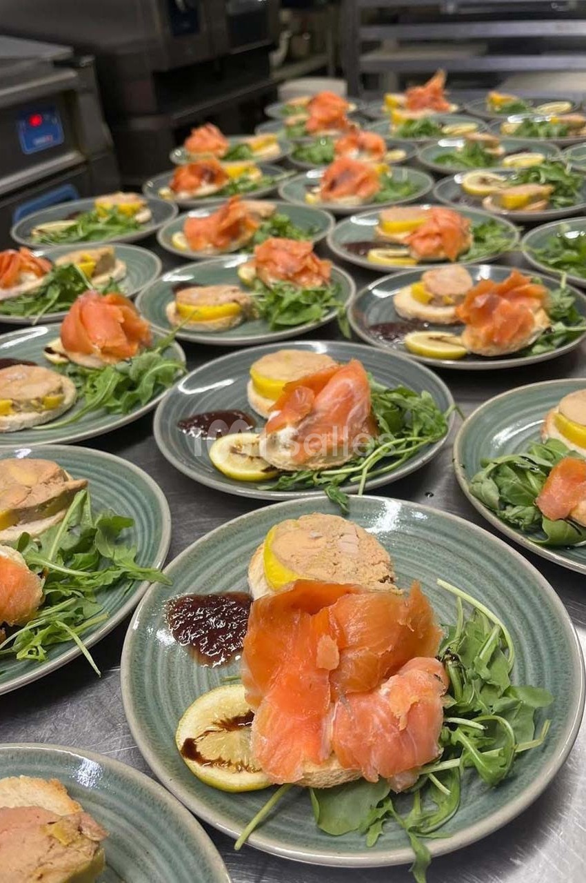 Assiettes garnies de saumon fumé, foie gras, citron, roquette et sauce, disposées sur un plan de travail en cuisine.