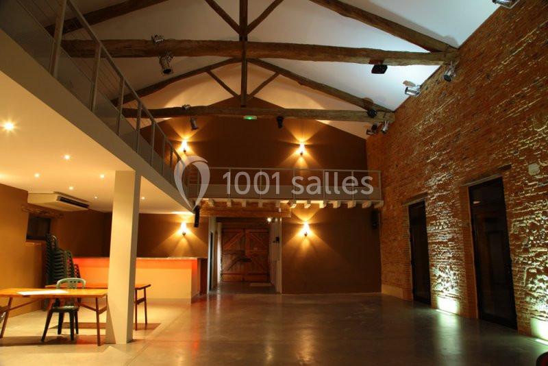 Salle spacieuse avec murs en briques, poutres apparentes, mezzanine et éclairage chaleureux.