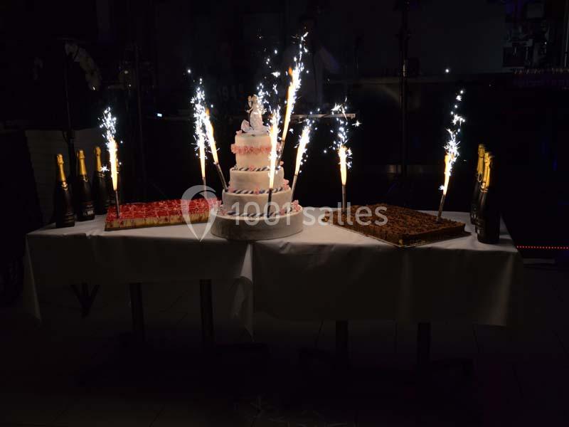 Gâteau de mariage à plusieurs étages entouré de desserts, décoré de cierges magiques allumés sur une table blanche.