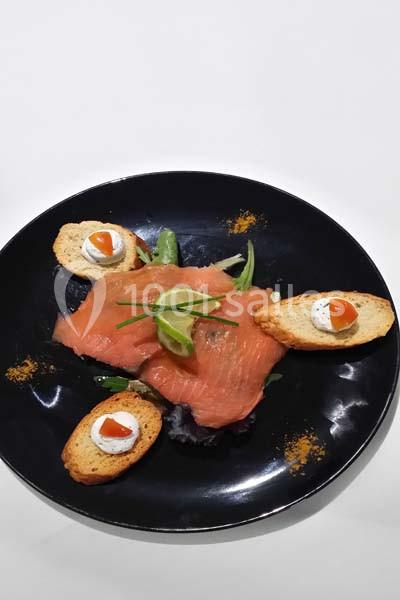 Assiette de saumon fumé avec tranches de citron vert, toasts garnis de crème et tomate, présentée sur un fond noir.
