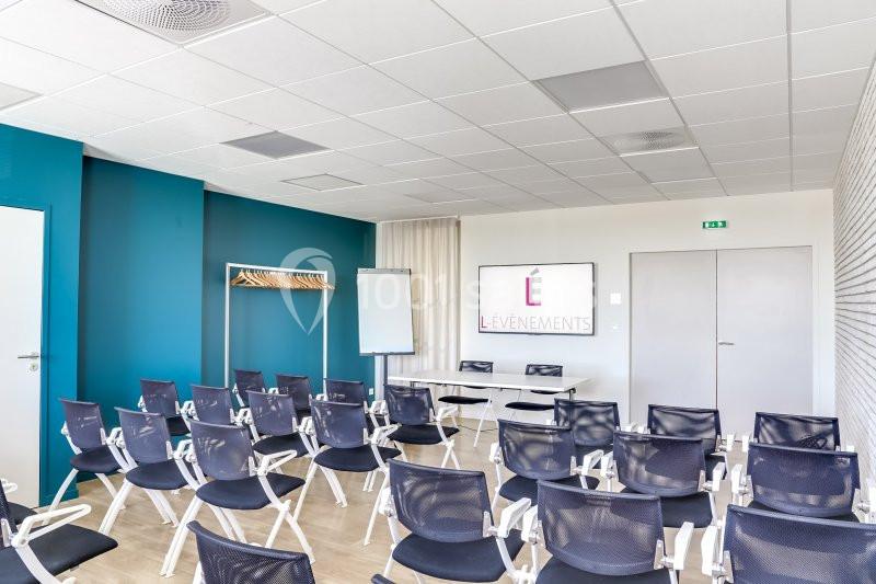 Salle de réunion lumineuse avec chaises noires, tableau blanc, paperboard et portemanteau contre un mur bleu.