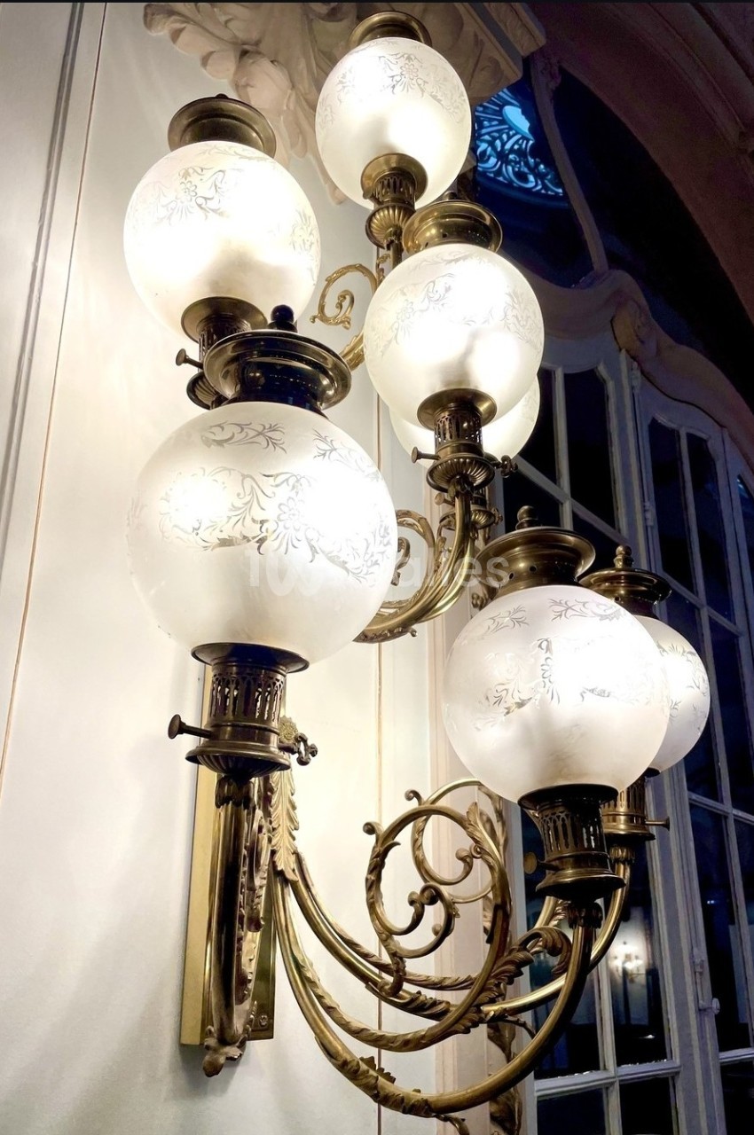 Applique murale en laiton avec globes en verre gravé, éclairant un intérieur aux moulures et grandes fenêtres.