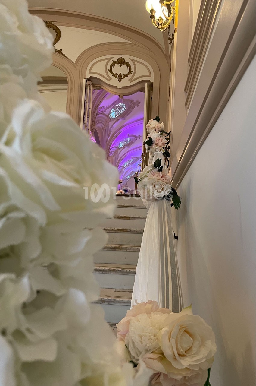 Escalier décoré de fleurs blanches et roses menant à une salle illuminée de lumières violettes.