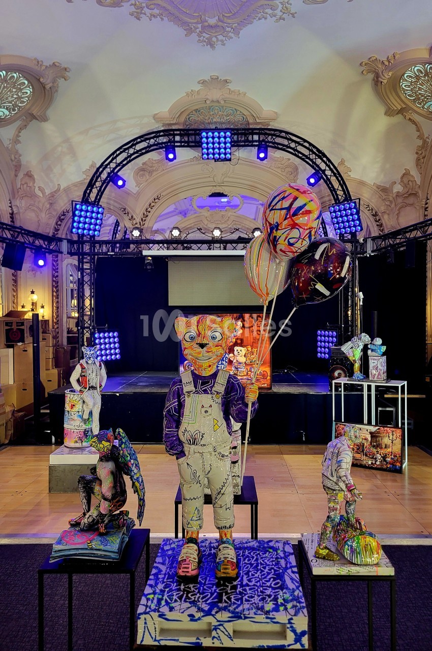 Statues colorées et artistiques exposées dans une salle ornée de moulures, éclairée par des projecteurs.