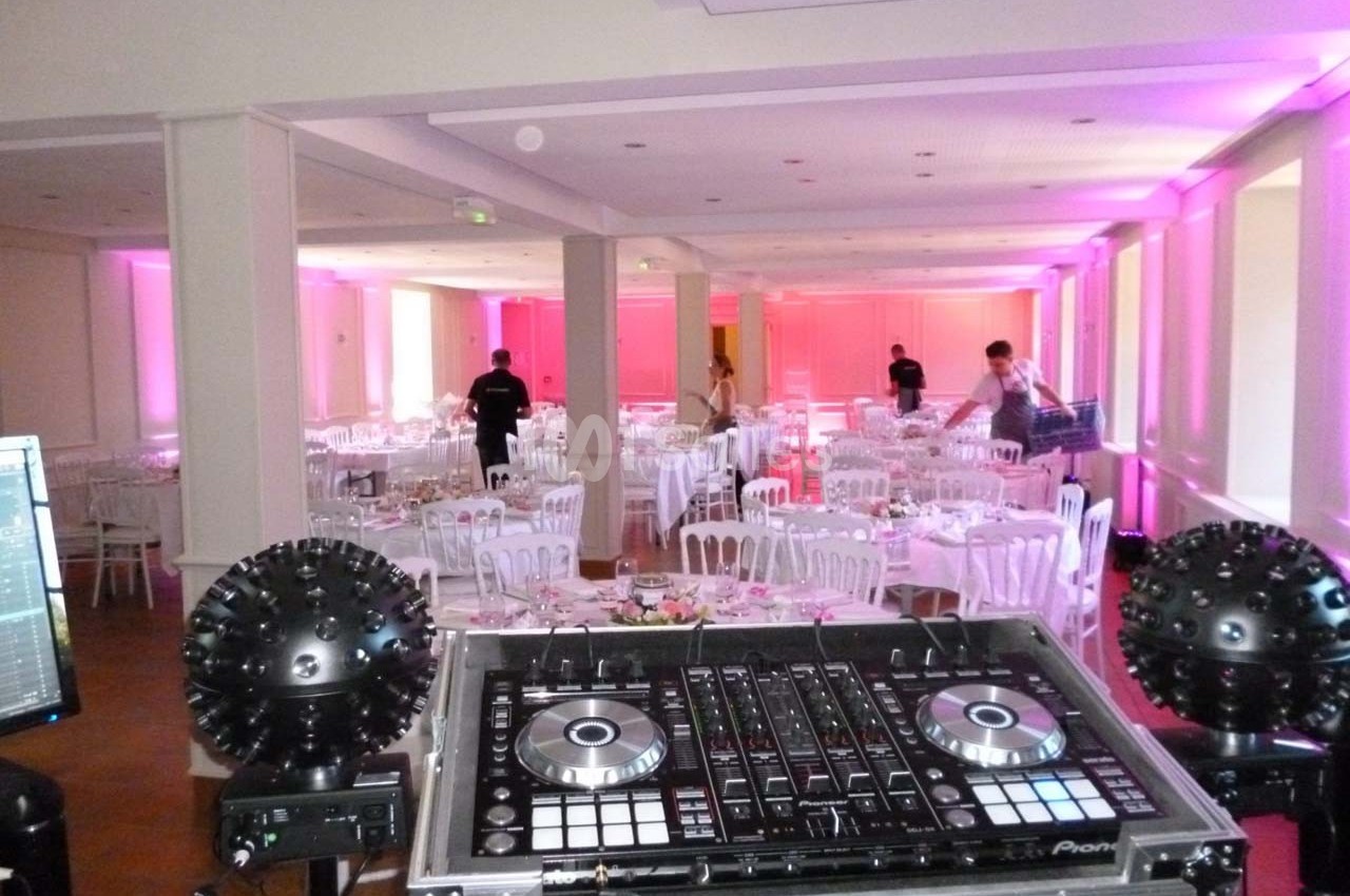 Salle de réception décorée avec des tables rondes, vue depuis une console de DJ au premier plan.