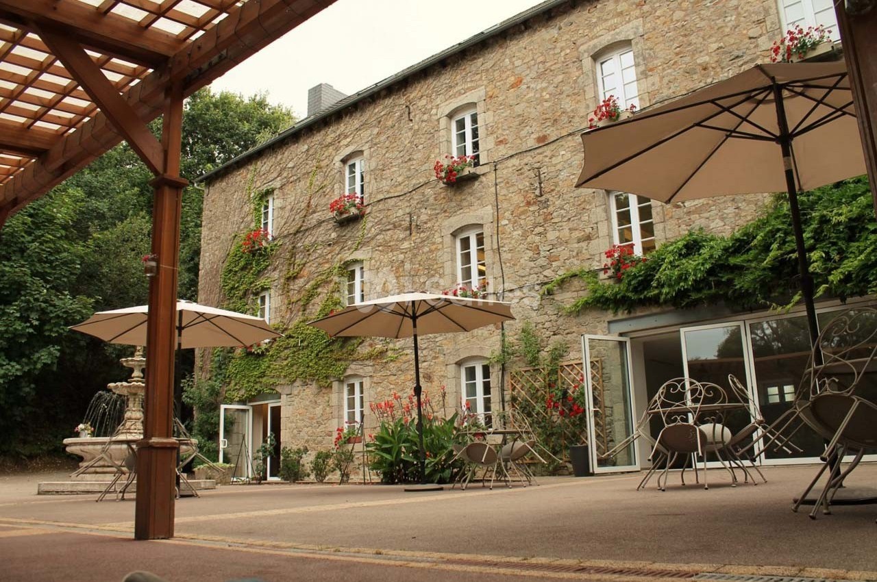 Cour intérieure avec fontaine, parasols, tables et chaises en fer forgé devant un bâtiment en pierre avec fenêtres fleuries.