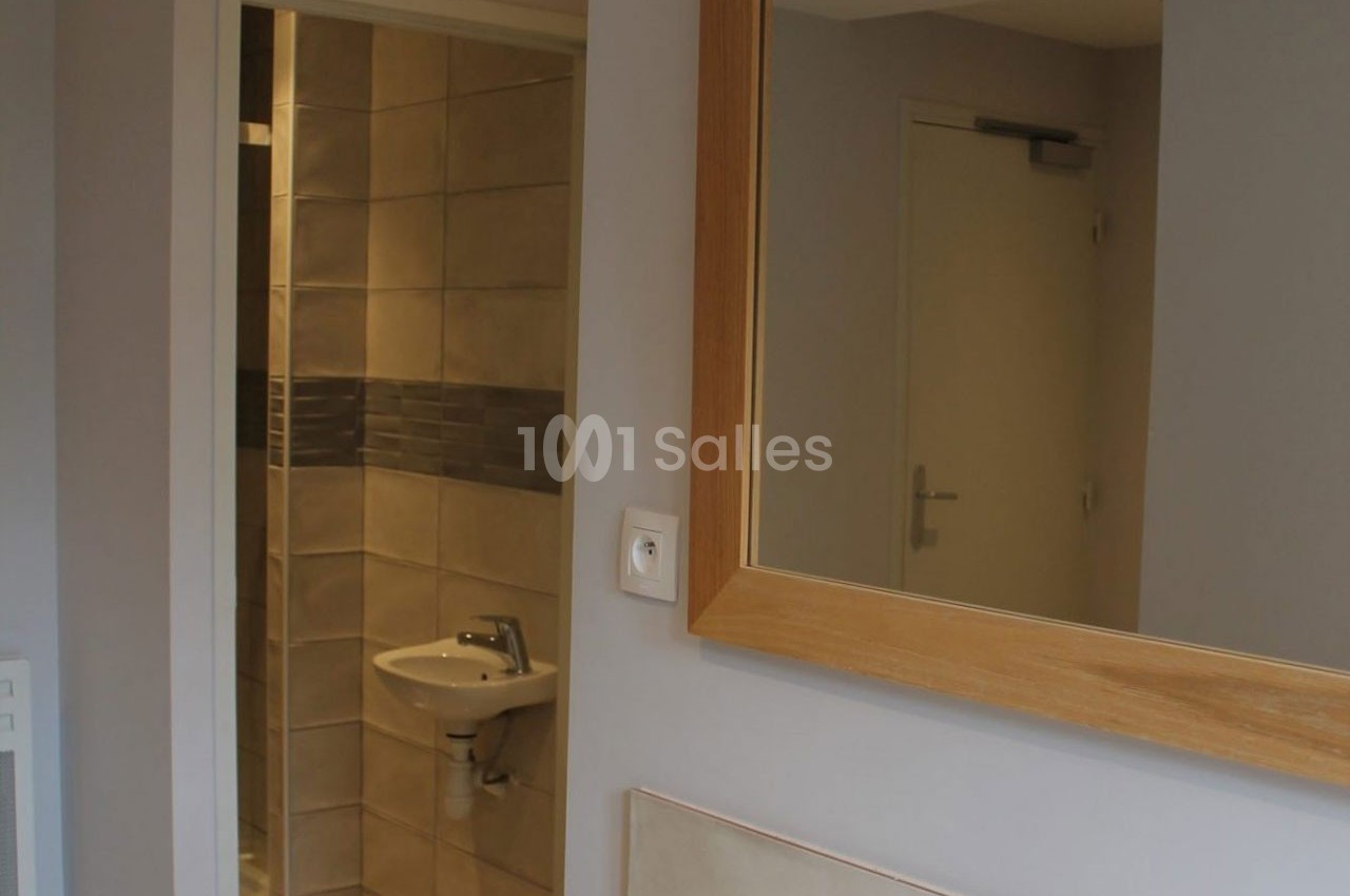 Vue d'une salle de bain avec un lavabo, un miroir encadré en bois et des carreaux beige et gris.
