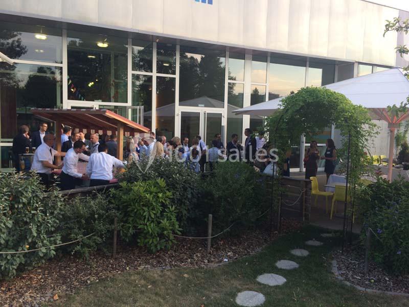 Groupe de personnes rassemblées dans un espace extérieur aménagé avec végétation, parasols et mobilier de jardin.