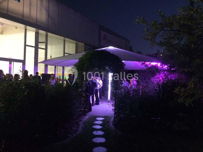 Un groupe de personnes rassemblé sous un grand parasol éclairé par des lumières violettes, dans un jardin de nuit.
