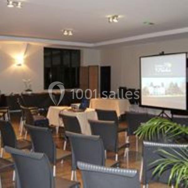 Salle de réunion avec des chaises disposées face à un écran de projection allumé, éclairage tamisé.
