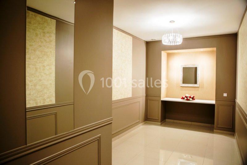 Couloir élégant avec murs beige, miroir encadré, table décorative et lustre moderne au plafond.