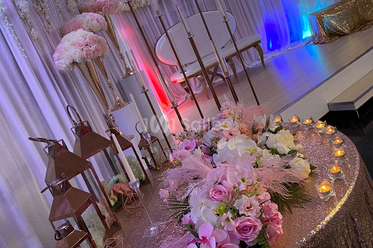 Décoration de salle avec table ornée de fleurs roses, lanternes cuivrées et bougies, devant une scène éclairée.