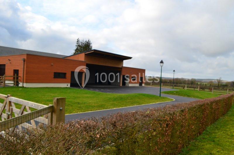 Bâtiment moderne en bois avec allée asphaltée, pelouse et haie, situé dans un environnement rural.