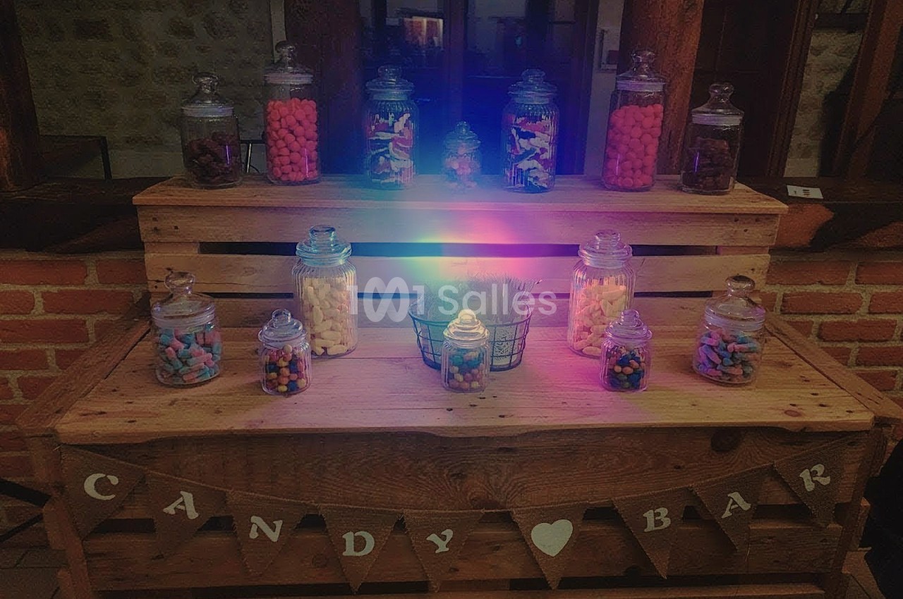 Buffet en bois décoré avec des bocaux de bonbons colorés et une guirlande ’Candy Bar’ dans un cadre rustique.