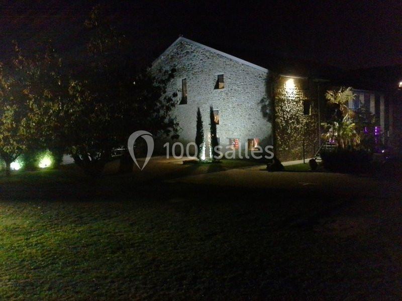 Bâtiment en pierre éclairé de nuit, entouré d'arbres et d'un jardin.