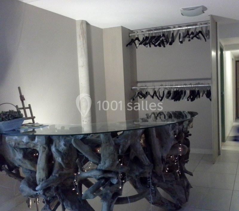 Comptoir en verre avec base en bois sculpté, entouré de portants métalliques avec des cintres noirs dans un espace moderne.
