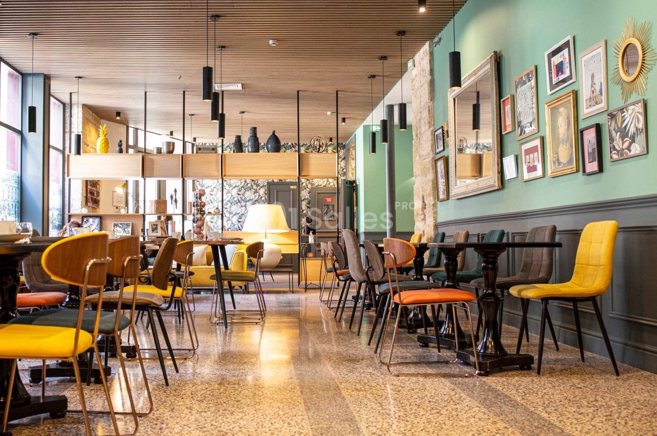 Salle de restaurant moderne avec chaises colorées, murs verts décorés de cadres et plafond en bois.
