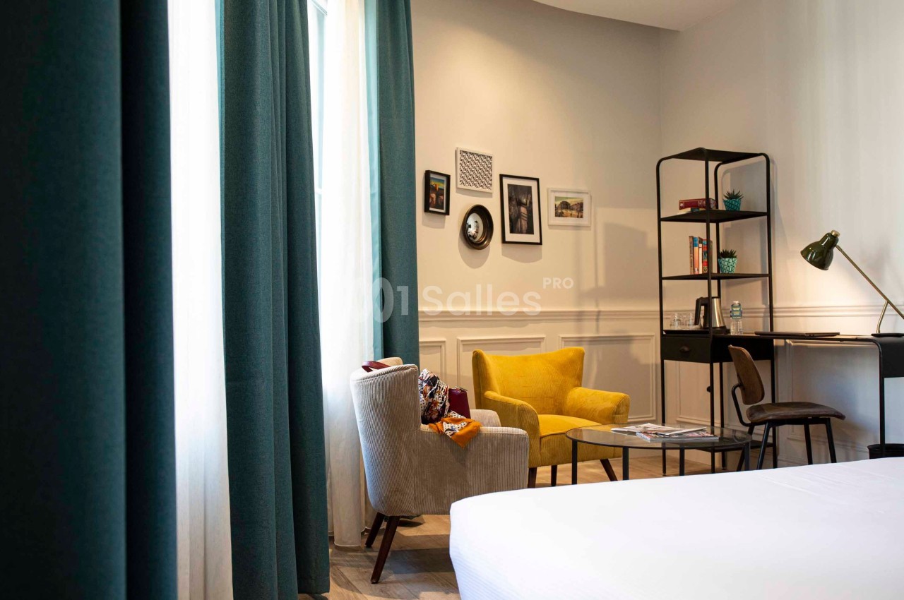 Coin salon lumineux avec fauteuils, table basse, bureau, étagères et décoration murale, près d'une fenêtre avec rideaux…