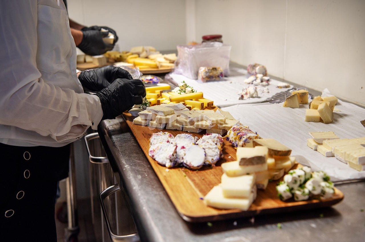 Personnes préparant un plateau de fromages variés sur un plan de travail en cuisine.