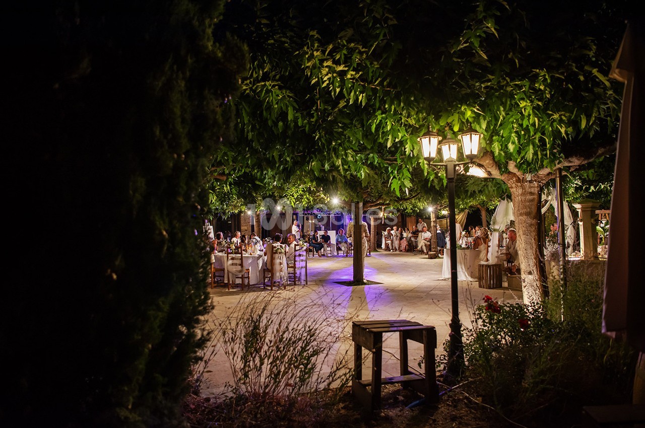 Dîner en plein air sous des arbres illuminés par des lampadaires, avec des invités assis autour de tables.