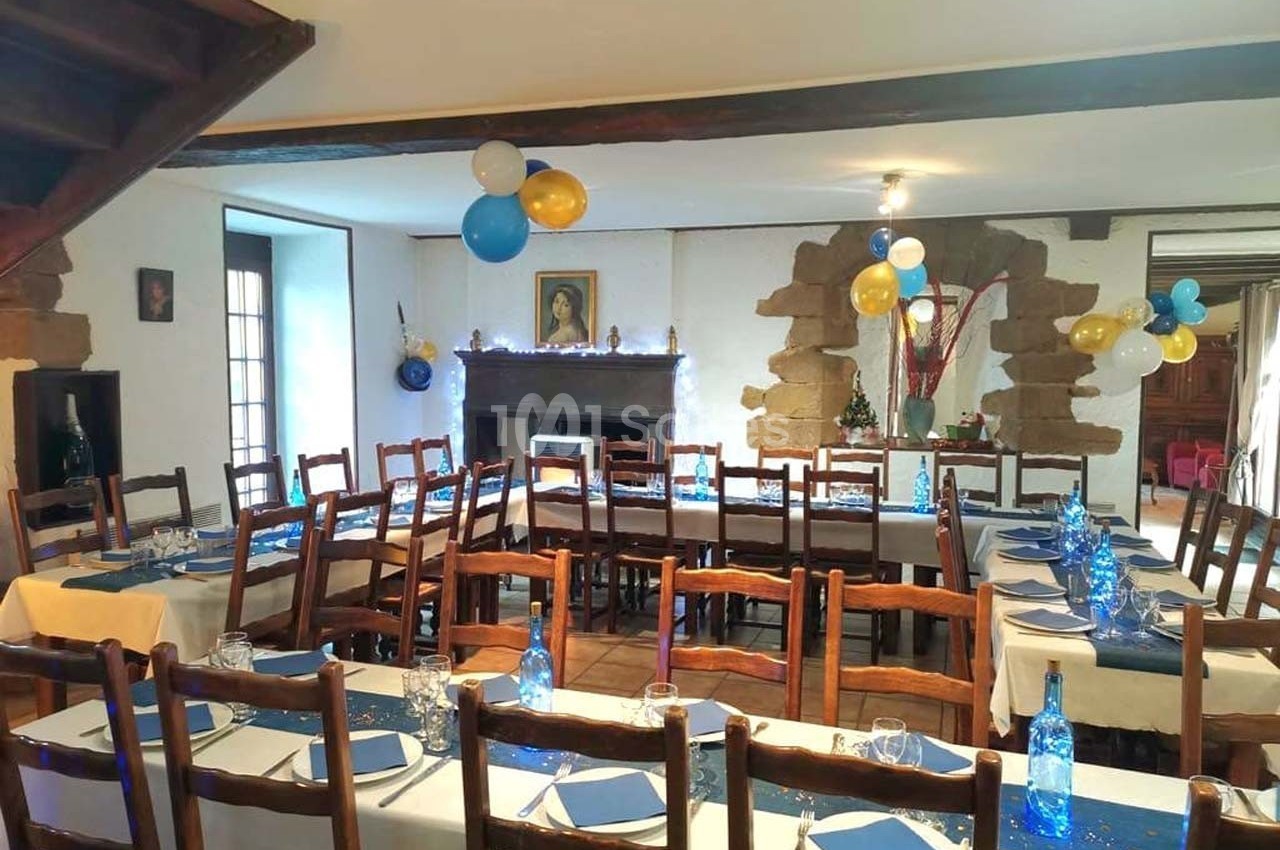 Salle de réception décorée avec des ballons et des tables dressées, alignées avec nappes blanches et chemins de table bleus.
