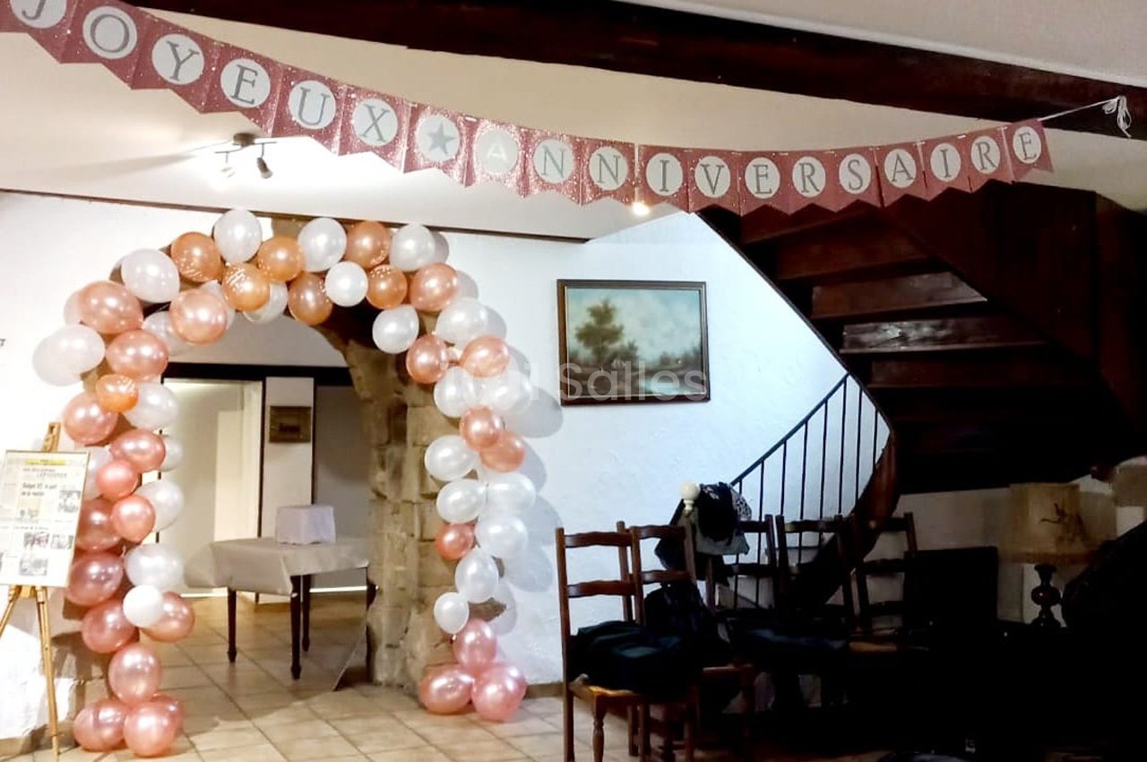 Décoration d'anniversaire avec arche de ballons blancs et roses, guirlande ’Joyeux Anniversaire’ et intérieur rustique.