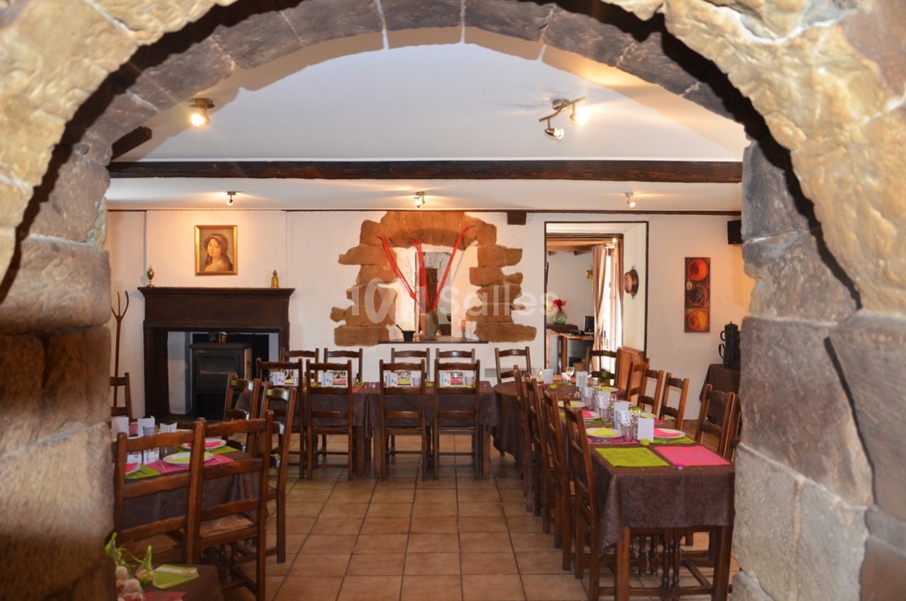 Salle à manger rustique avec tables en bois dressées, murs en pierre et décorations chaleureuses.