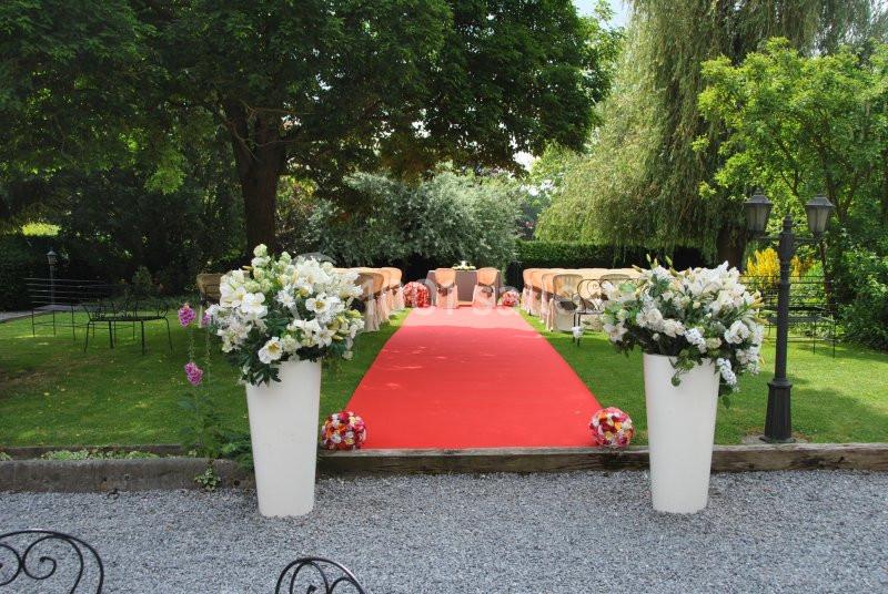 Allée centrale avec tapis rouge bordée de chaises et décorations florales, menant à un espace de cérémonie en plein air.