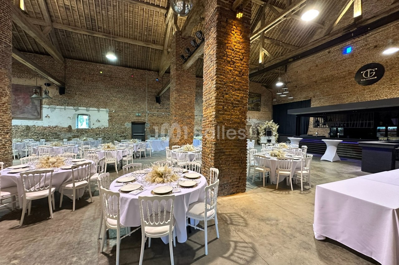 Salle de réception avec murs en briques, tables rondes dressées, chaises blanches et éclairage chaleureux.