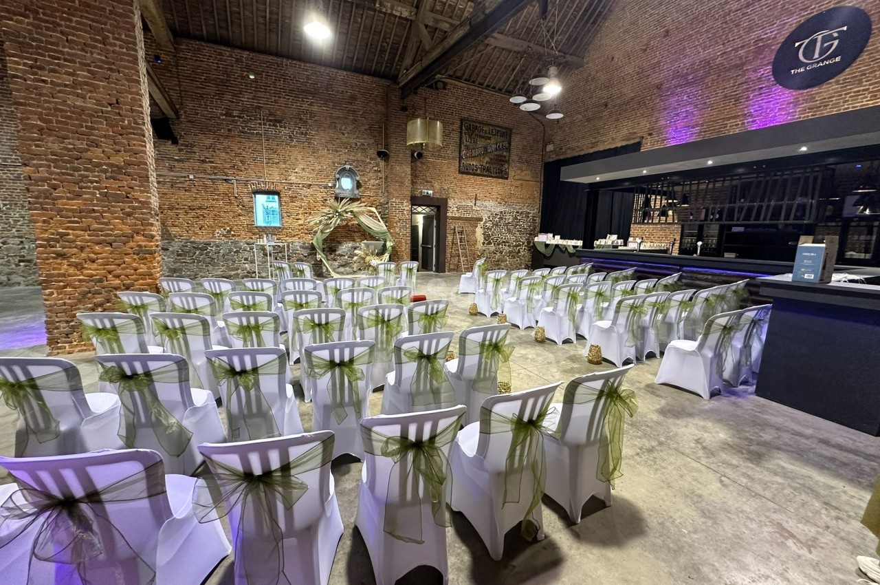Salle de réception avec des chaises blanches décorées de rubans verts, disposées face à un bar moderne dans un cadre en…