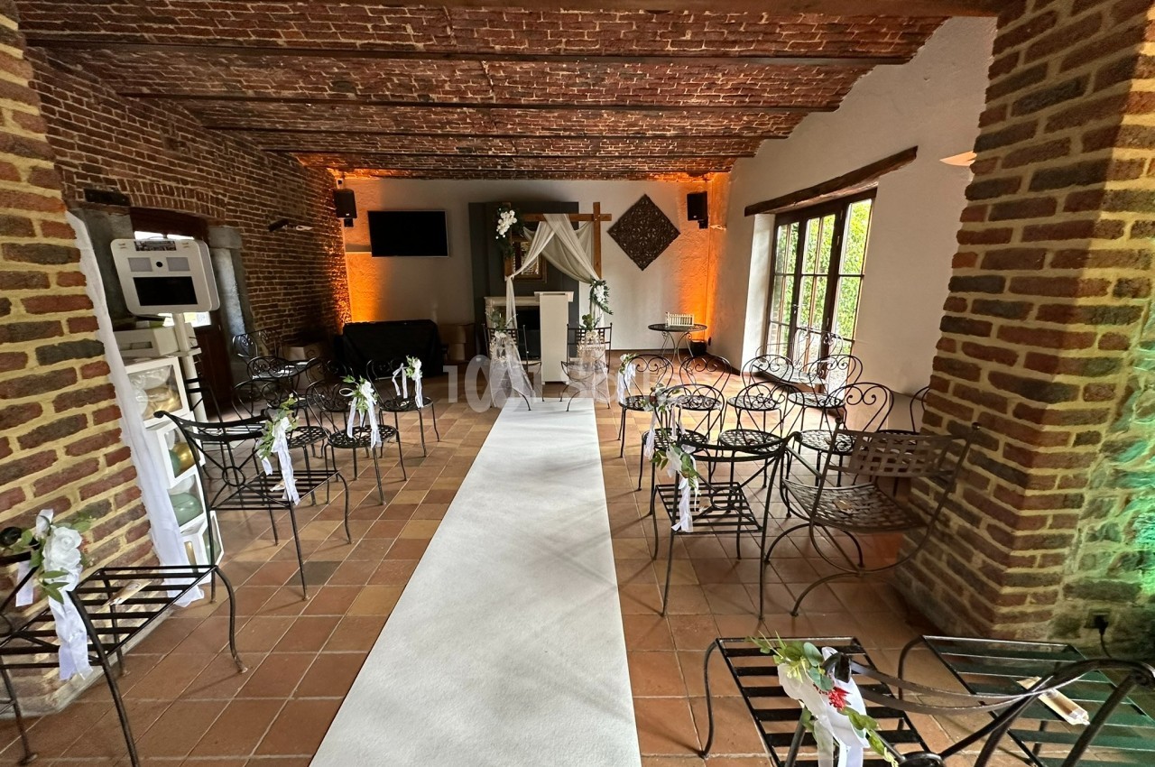 Salle décorée pour une cérémonie, avec chaises en fer forgé, allée centrale blanche et autel orné de fleurs.