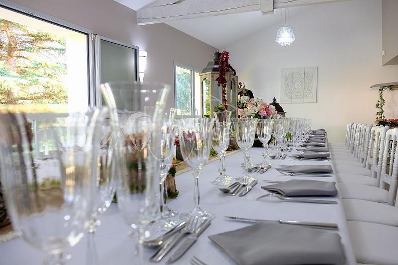Table élégamment dressée avec nappes blanches, verres en cristal, serviettes grises et décorations florales.