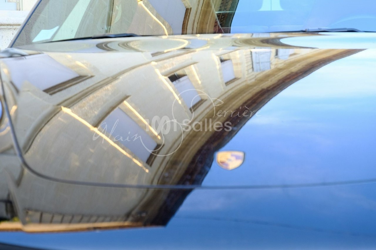 Reflet d'un bâtiment sur le capot brillant d'une voiture noire stationnée.