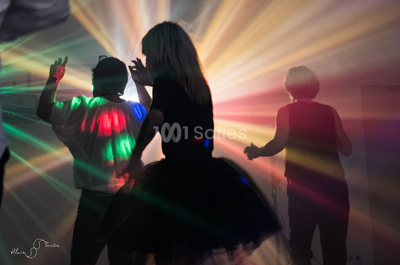 Personnes dansant dans une ambiance sombre avec des faisceaux lumineux colorés traversant la pièce.