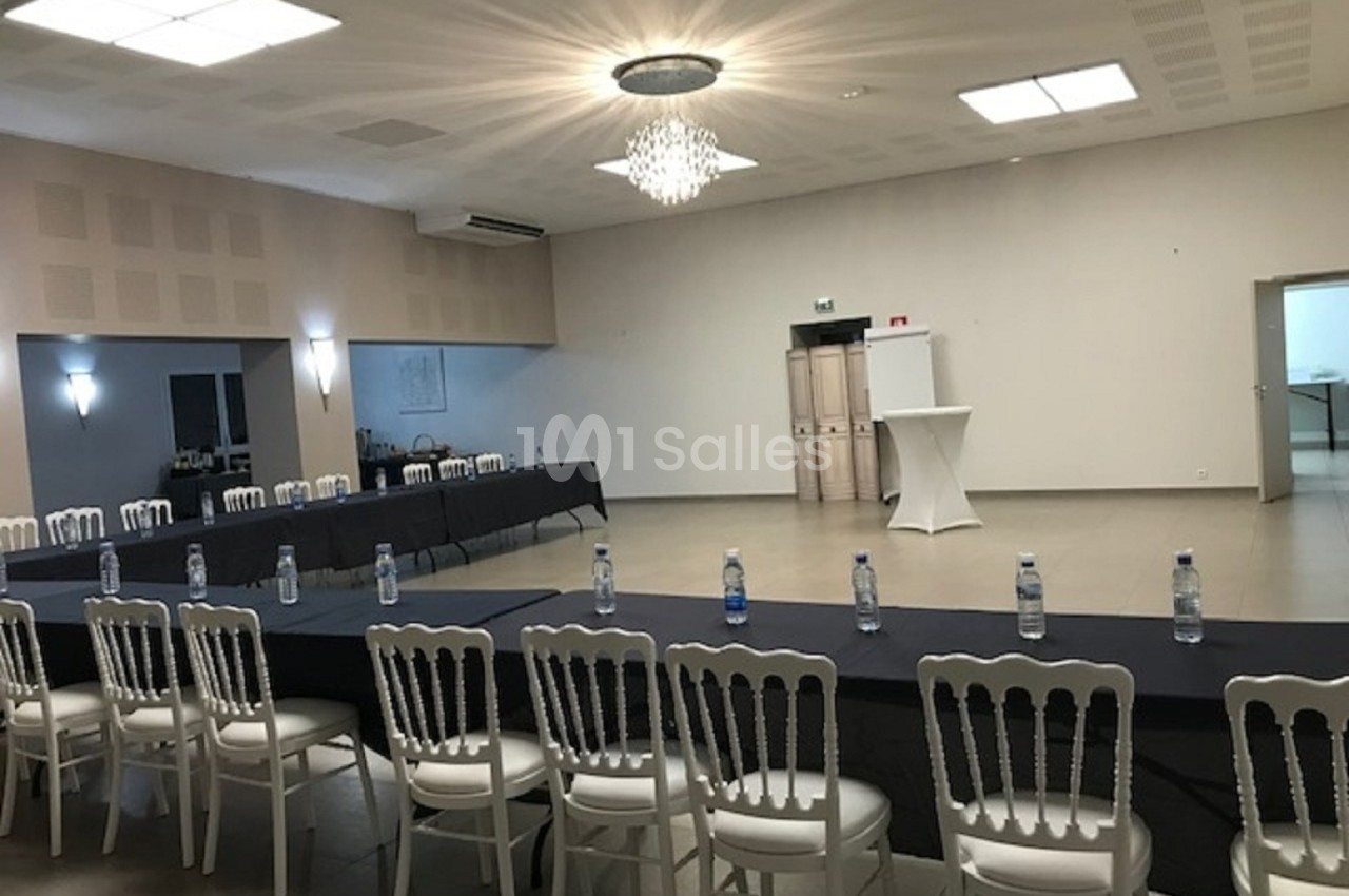 Salle de réunion lumineuse avec des tables disposées en U, des chaises blanches et des bouteilles d'eau alignées.