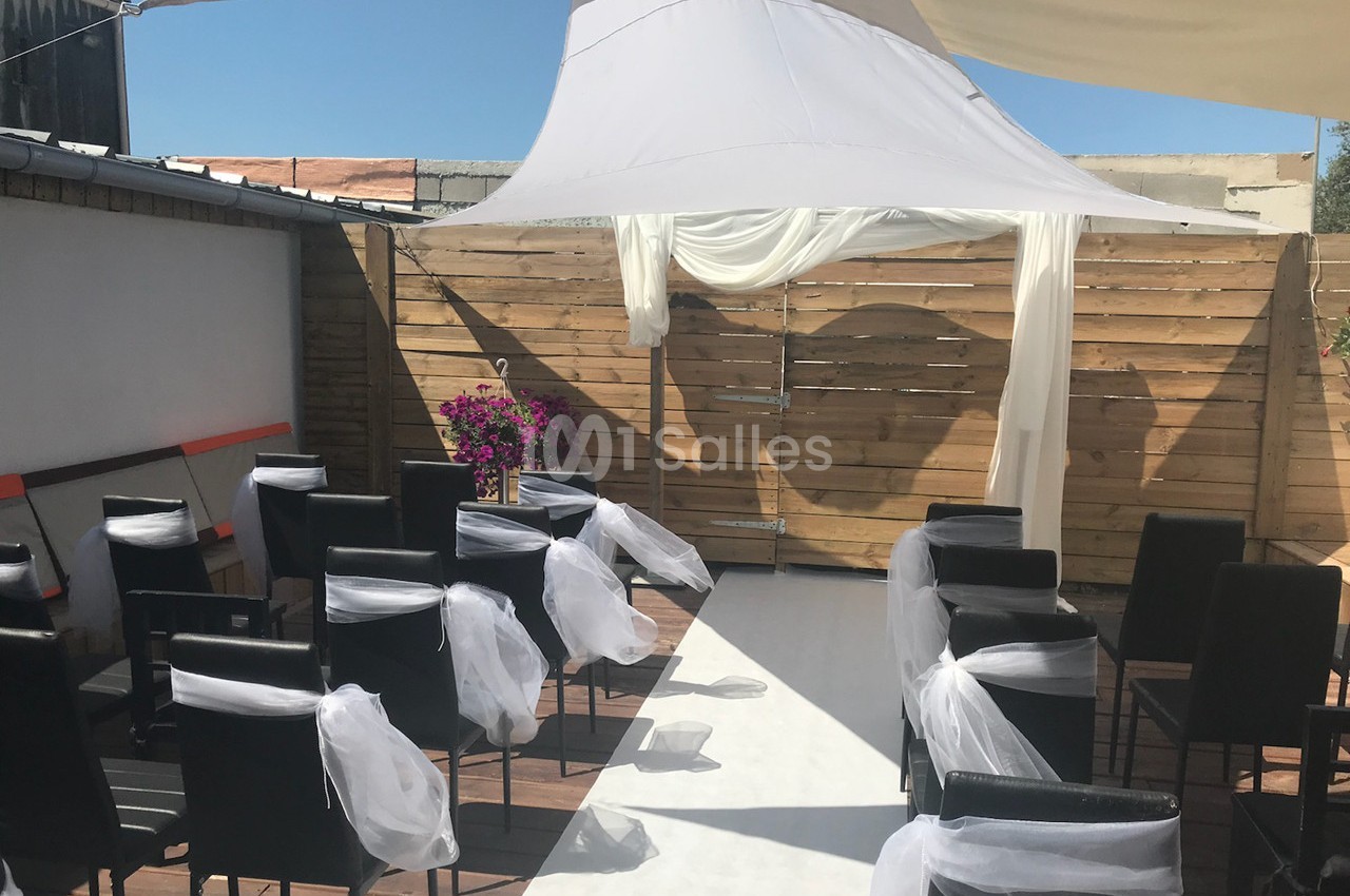 Chaises noires décorées de voiles blancs disposées devant une arche en bois sous une tente blanche en extérieur.