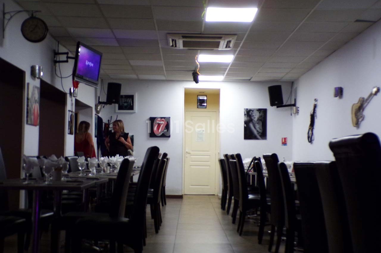 Salle de restaurant avec tables dressées, chaises noires, décorations murales et deux personnes discutant au fond.