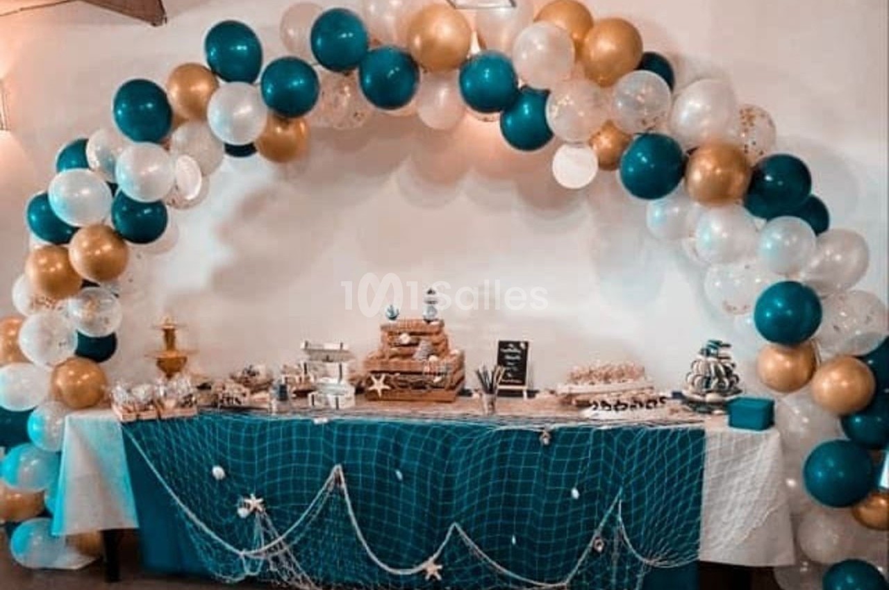 Table décorée pour une fête avec des desserts variés, ornée d’un filet marin et d’une arche de ballons bleus, dorés et…