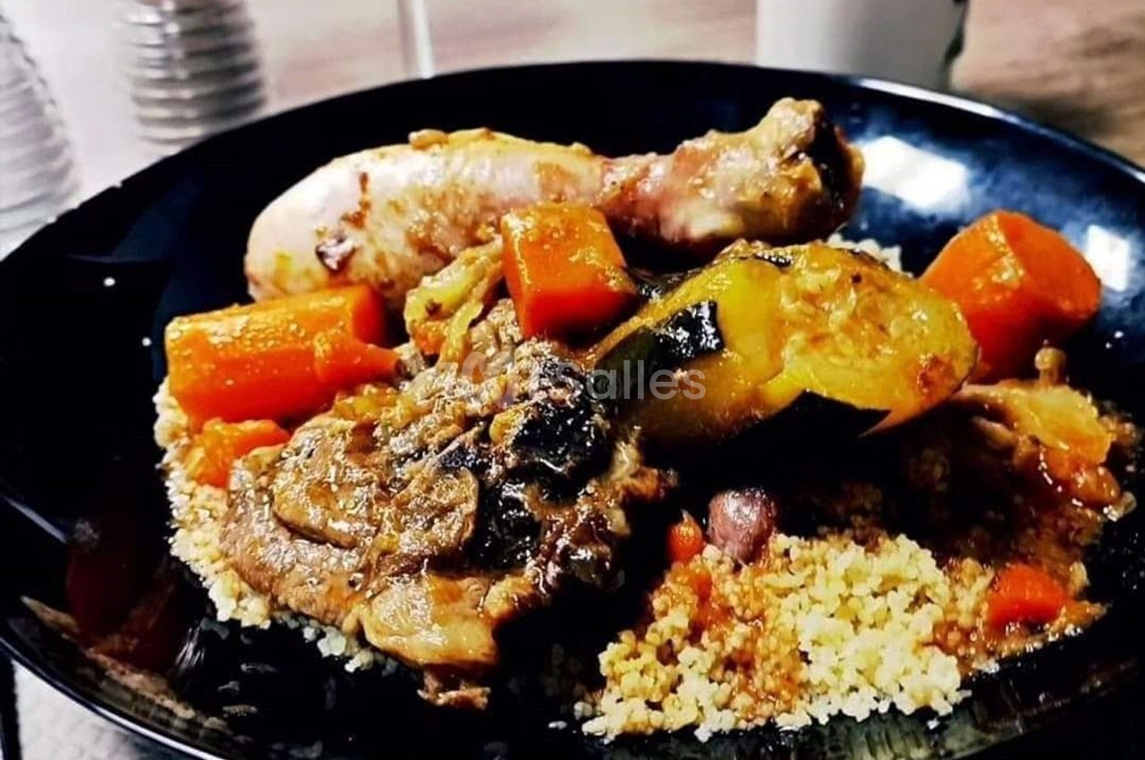 Assiette de couscous garnie de morceaux de poulet, carottes et courgettes, servie sur une table en intérieur.