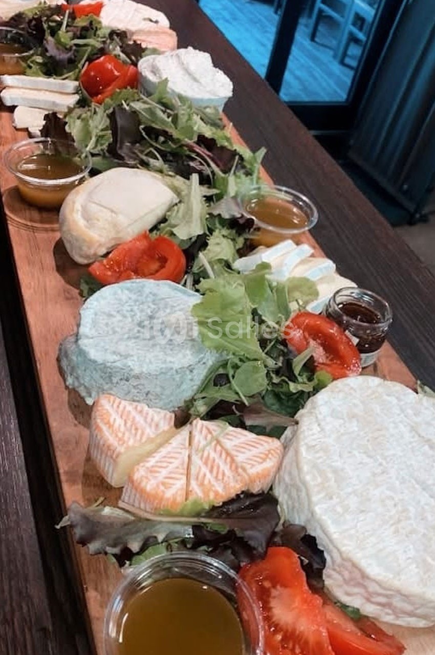 Plateau en bois garni de fromages variés, salades, tomates et petites coupelles de sauce.