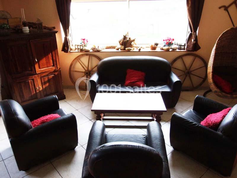 Salon avec fauteuils en cuir noir, table basse en bois, armoire ancienne et fenêtre laissant entrer la lumière.